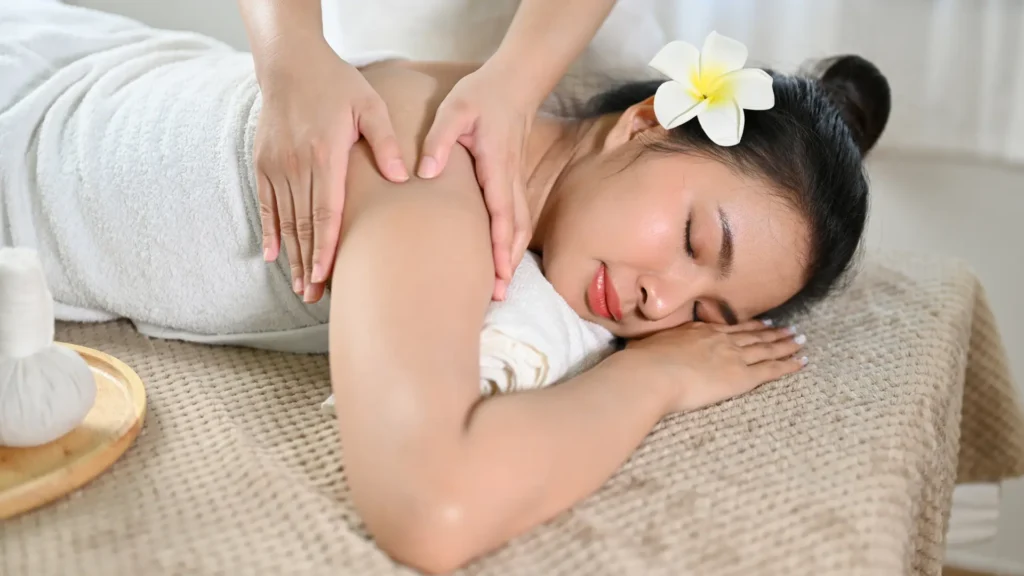 Woman lying on her stomach as a massage therapist applies pressure to her shoulders during a shiatsu massage session.