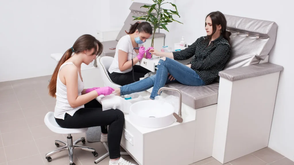 Two specialists giving manicure and pedicure services to a female Client